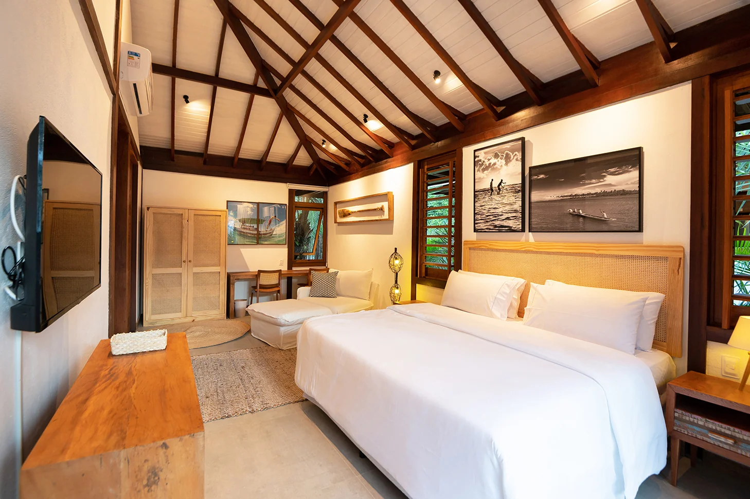 Suíte 3 com cama de casal, chaise, televisão e teto alto com vigas de madeira