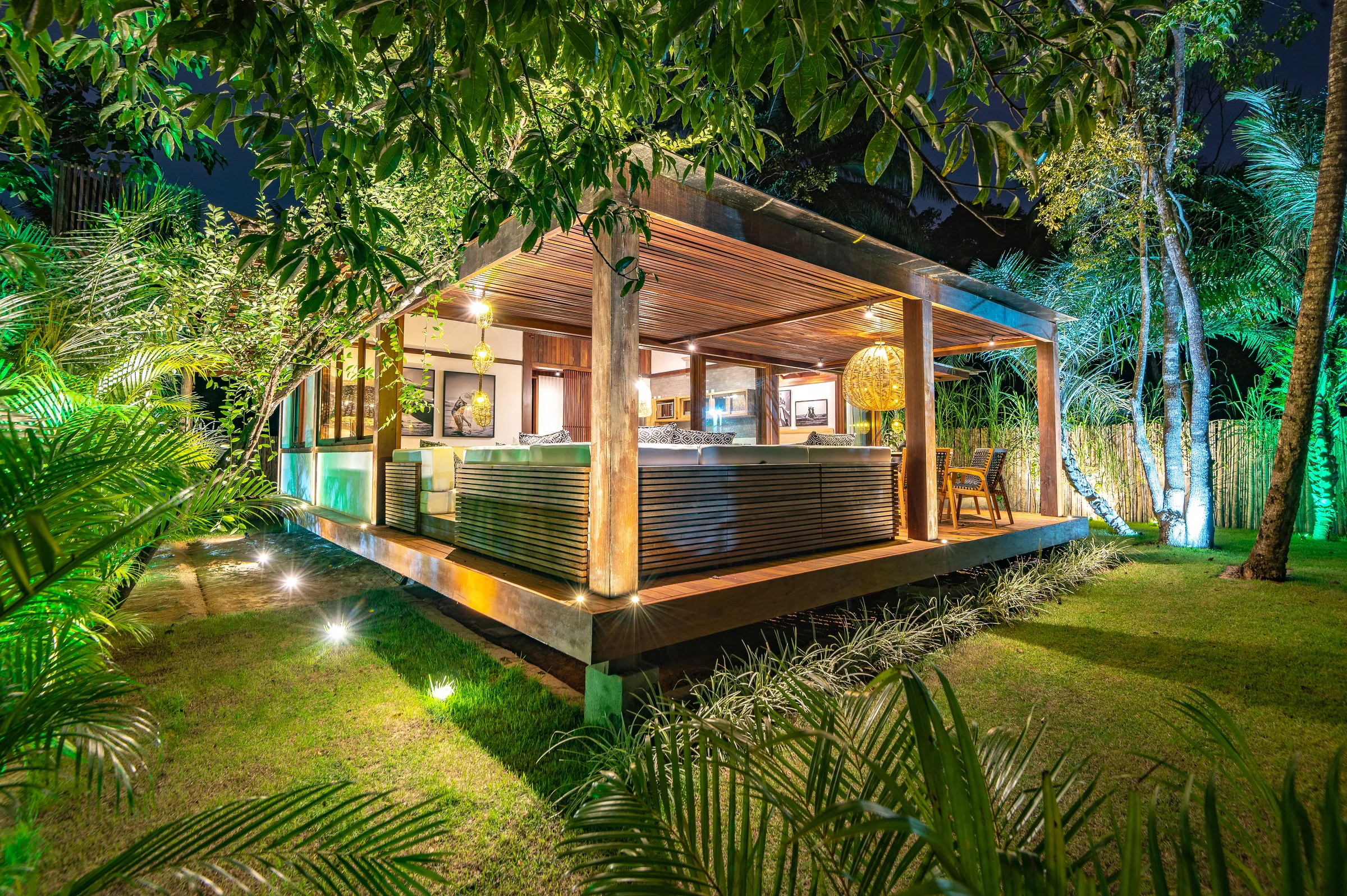 Villa 3 iluminada ao anoitecer entre o gramado, as palmeiras e o jardim